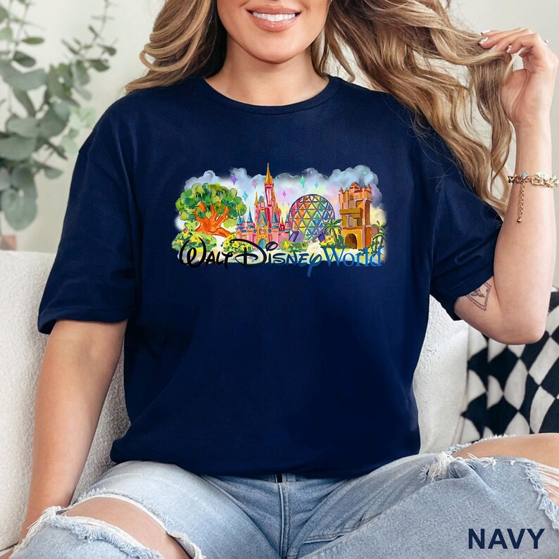 May include: A navy blue short-sleeve t-shirt featuring a colorful graphic print of the Walt Disney World theme park landmarks, including the castle, the geodesic sphere, and the tree of life, with the text Walt Disney World printed below.