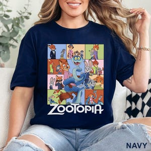 May include: A navy blue t-shirt featuring a grid of various Zootopia character illustrations, including Nick Wilde and Judy Hopps, with a large blue snake in the centre and the white text Zootopia printed prominently at the bottom of the graphic.