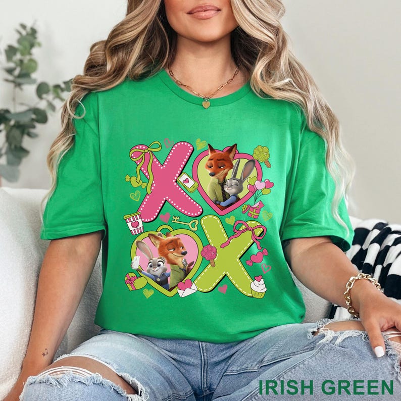 Peut inclure: Un t-shirt vert vif avec une impression graphique repr&eacute;sentant deux animaux de dessin anim&eacute;, un renard et un lapin, &agrave; l'int&eacute;rieur de c&oelig;urs. Le motif inclut de grandes lettres roses et jaunes formant XOXO, orn&eacute;es de petits c&oelig;urs et rubans.