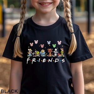May include: Black t-shirt with the word "FRIENDS" in white and colourful dots. Above the word are cartoon characters and Mickey Mouse-shaped balloons. The word "BLACK" is printed at the bottom of the shirt.