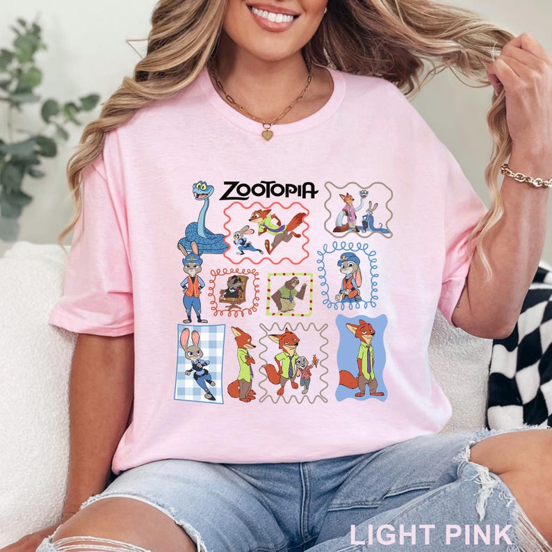 K&ouml;nnte beinhalten: Ein hellrosa T-Shirt mit einem Grafikdruck verschiedener Zootopia-Figuren in einzelnen Rahmen, darunter Judy Hopps und Nick Wilde. Der Text Zootopia ist in Schwarz oben mittig auf dem Grafikdesign auf der Vorderseite des T-Shirts gedruckt.