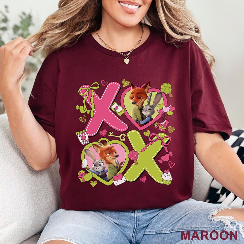 Peut inclure: Un t-shirt bordeaux avec une impression graphique affichant le texte XOXO en grandes lettres roses et vert citron. Le motif comprend des illustrations d'un renard et d'un lapin dans des c&oelig;urs, entour&eacute;s de petits symboles de c&oelig;urs, cadeaux et friandises.
