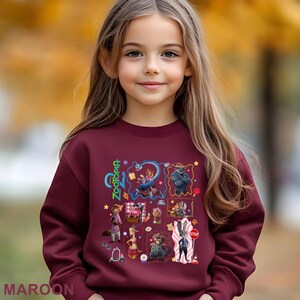 May include: Maroon sweatshirt featuring a colorful graphic of characters from the animated movie "Zootopia." The design includes the word "Zootopia" in green and various animal characters in a collage-style arrangement. The word "MAROON" is printed at the bottom.