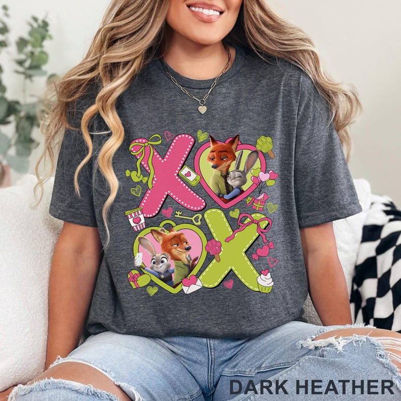 Peut inclure: Un t-shirt gris chin&eacute; fonc&eacute; avec une impression graphique des personnages Nick Wilde et Judy Hopps de Zootopie. Le motif comprend de grandes lettres roses et vert citron formant XOXO, des c&oelig;urs roses, des petits cadeaux, des cupcakes et des bonbons.