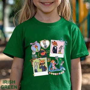 May include: A short-sleeved emerald green t-shirt featuring a graphic print of various Zootopia characters. The design includes multiple polaroid-style frames and heart-shaped borders containing illustrations of Nick Wilde and Judy Hopps.