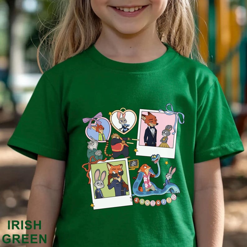 May include: A short-sleeved emerald green t-shirt featuring a graphic print of various Zootopia characters. The design includes multiple polaroid-style frames and heart-shaped borders containing illustrations of Nick Wilde and Judy Hopps.