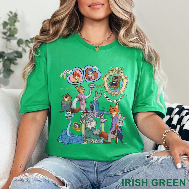 May include: Irish green t-shirt featuring a colorful graphic of cartoon characters. The design includes framed portraits and various animal figures. The word "ZOOTOPIA" is also visible in the design.