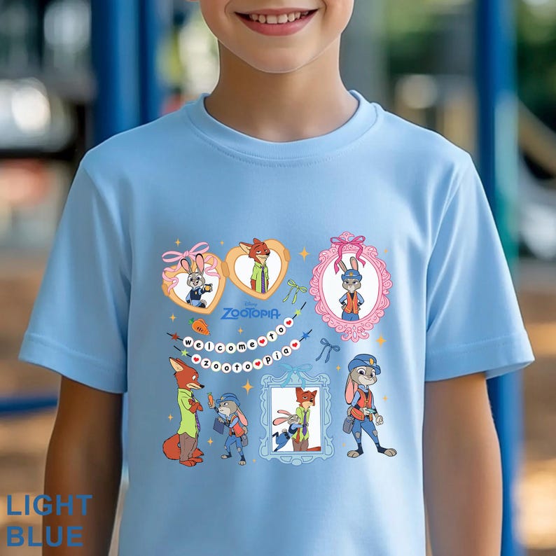 Pode incluir: Camiseta azul claro com personagens de desenhos animados do filme Zootopia. A camisa apresenta imagens emolduradas de personagens como Judy Hopps e Nick Wilde, juntamente com as palavras "Zootopia" e "Welcome to Zootopia".