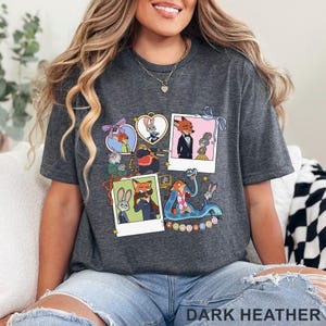 May include: A dark heather gray t-shirt featuring a graphic print of Zootopia characters in various frames and polaroid-style photos. The design includes Judy Hopps, Nick Wilde, and other movie figures with the text Zootopia at the bottom.