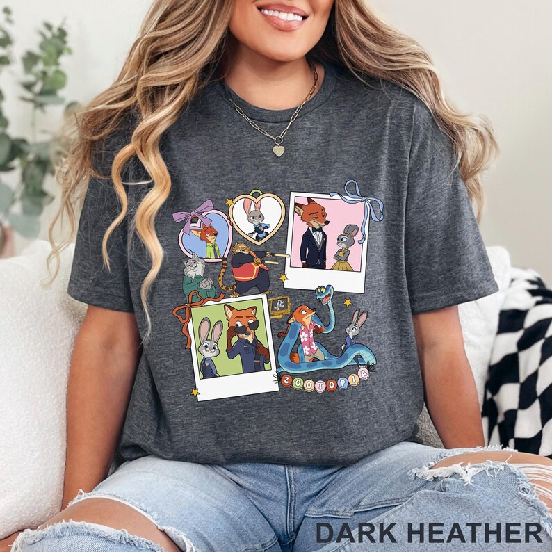 May include: A dark heather gray t-shirt featuring a graphic print of Zootopia characters in various frames and polaroid-style photos. The design includes Judy Hopps, Nick Wilde, and other movie figures with the text Zootopia at the bottom.