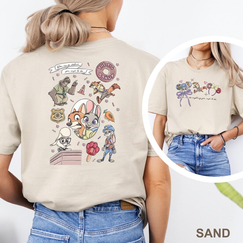 May include: A sand-colored t-shirt featuring a Zootopia-themed graphic print. The back displays various characters, a police badge, a donut, and a carrot. The front chest area shows smaller icons including mouse ears and the text You can be anything you wish to be.
