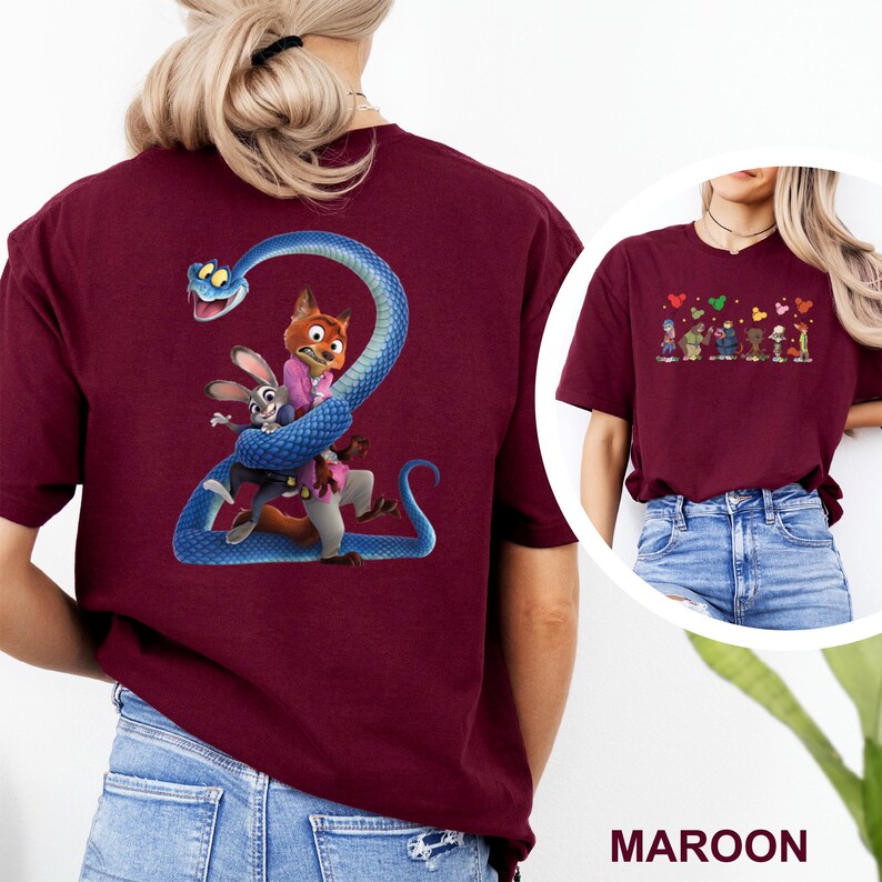 K&ouml;nnte beinhalten: Burgunderfarbenes T-Shirt mit einem Cartoon-Bild eines Fuchses, eines Kaninchens und einer Schlange. Der Fuchs tr&auml;gt einen rosa Anzug, und das Kaninchen tr&auml;gt einen blauen Anzug. Die Schlange ist blau. Das Shirt hat auch ein kleineres Bild von Cartoon-Figuren mit Herzen.