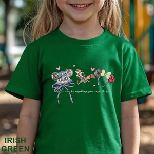 May include: An Irish green short-sleeved t-shirt featuring a graphic print of two cartoon characters, mouse-ear headbands, and the text "You can be anything you wish to be" in a cursive white font centered on the chest area of the garment.