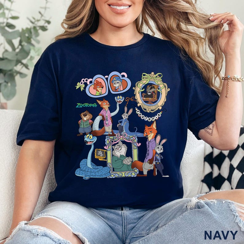 May include: Navy blue t-shirt featuring a colorful graphic of characters from the animated film Zootopia. The design includes various animal characters in ornate frames and the word "Zootopia" in green. The shirt is a comfortable, casual style.