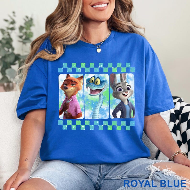 May include: Royal blue t-shirt featuring a graphic of three cartoon characters: a fox, a snake, and a rabbit. The graphic is framed with a checkered pattern in green and blue. The shirt is a solid royal blue color.