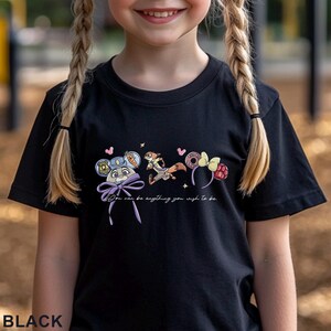 May include: A black t-shirt featuring a graphic print of a rabbit character wearing a police hat, a fox character, and two sets of mouse-style ears. The text "You can be anything you wish to be" is printed below the characters in a white script font.