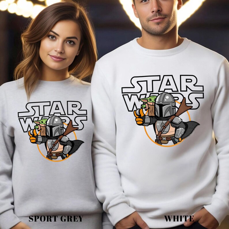 May include: Sport grey and white sweatshirts featuring a Star Wars design. The design includes the Star Wars logo, a cartoon Mandalorian character, and Grogu. The sweatshirts are long-sleeved.