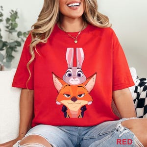 May include: A red t-shirt with a cartoon illustration of a fox and a rabbit. The fox is orange and the rabbit is grey. The word "RED" is printed in the bottom right corner of the image.