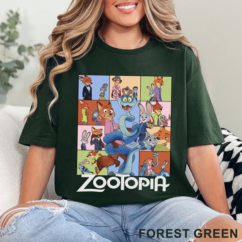 May include: A forest green short-sleeve t-shirt featuring a grid of various Zootopia character illustrations, including Nick Wilde and Judy Hopps, with a large blue snake in the centre and the word Zootopia printed in white text at the bottom.