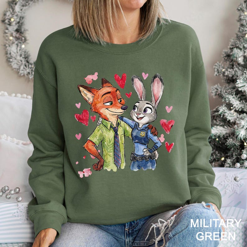 May include: Military green sweatshirt with a watercolour illustration of Nick Wilde and Judy Hopps from Zootopia, surrounded by pink hearts. Nick wears a green shirt and tie, Judy a police uniform. The text "MILITARY GREEN" is at the bottom.