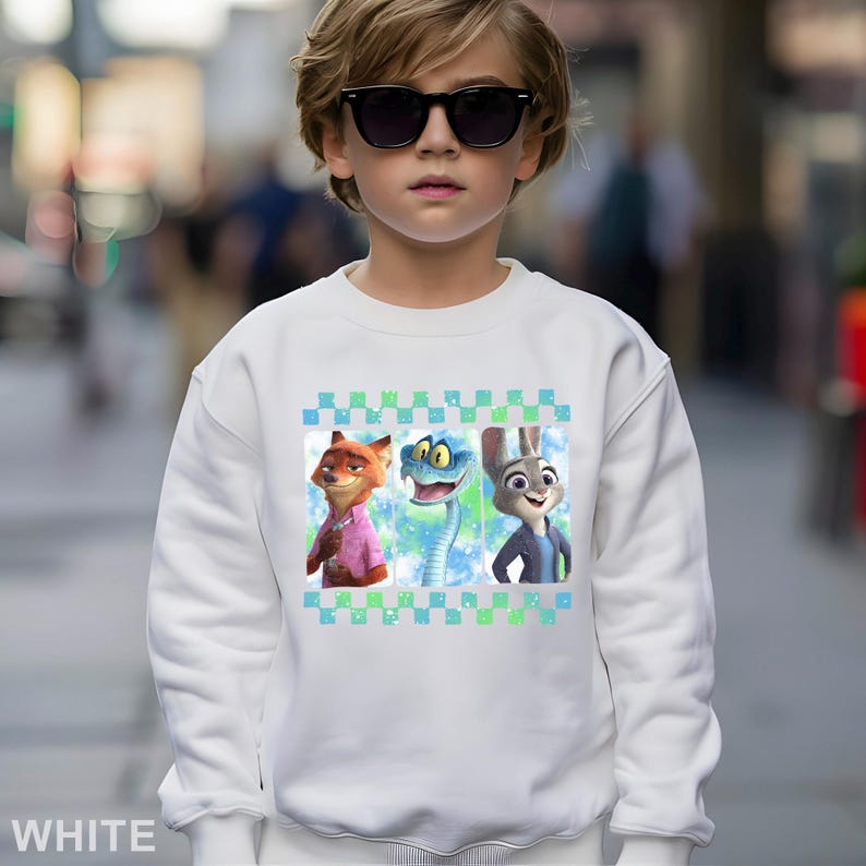 May include: White sweatshirt with a design of three cartoon characters: a fox in a pink shirt, a blue snake, and a rabbit in a blue jacket. The design is framed by a green and blue checkered pattern. The sweatshirt is worn by a child wearing sunglasses.