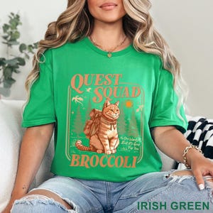 May include: Irish green t-shirt with a graphic featuring a cat wearing a backpack, the words "QUEST SQUAD BROCCOLI", and the text "No One Wants It, But It's Good For You". The shirt is a crew neck.