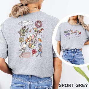 May include: A sport grey t-shirt featuring a back graphic with various cartoon animal characters, a donut, a badge, a carrot, and a paw-shaped popsicle. The text reads, "You can be whatever you wish to be." A smaller version of the graphic is on the front.