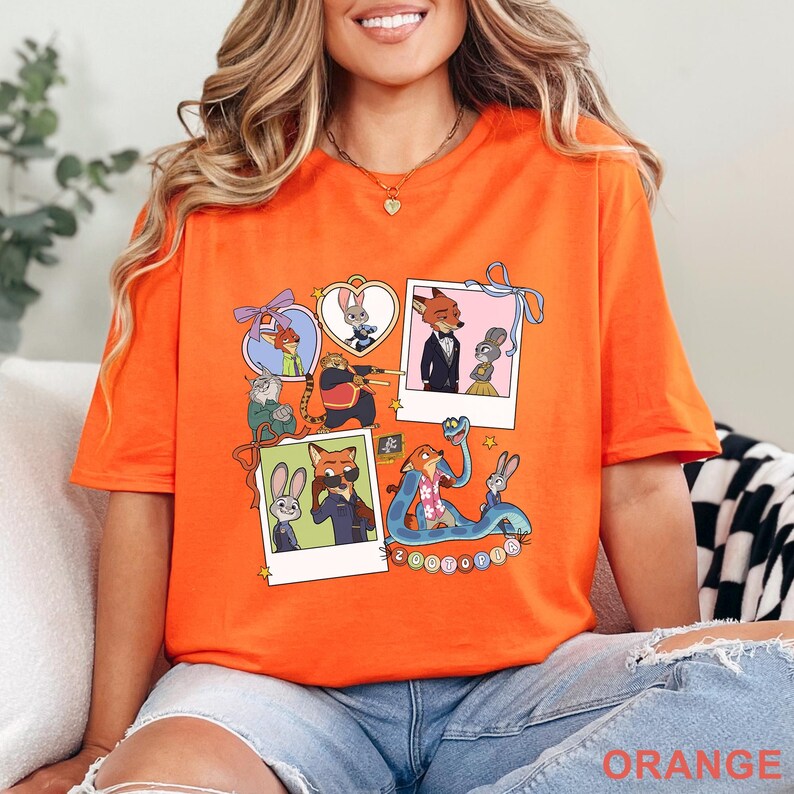 May include: An orange short-sleeve t-shirt featuring a graphic print of Zootopia characters. The design includes multiple polaroid-style frames and heart-shaped borders containing illustrations of Nick Wilde, Judy Hopps, and other characters, with the text Zootopia.