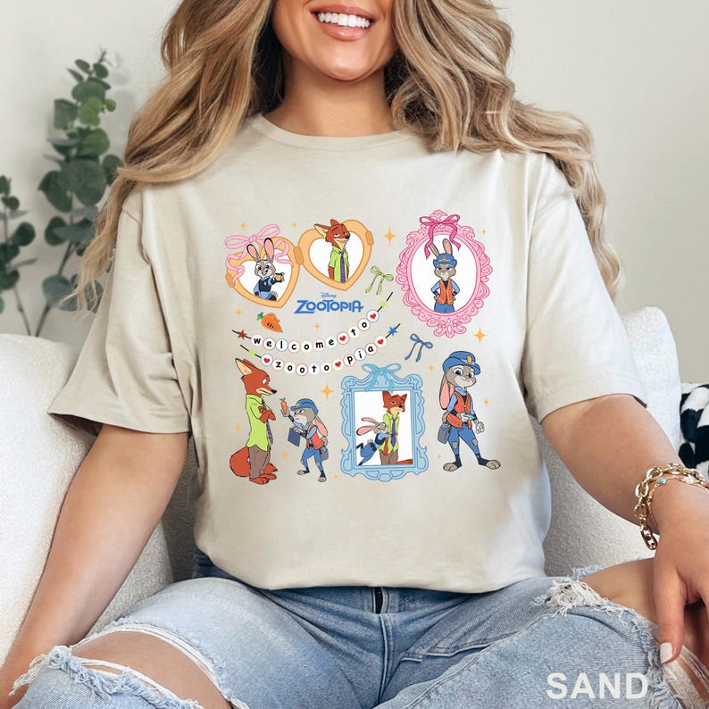 Pode incluir: Camiseta cor de areia com personagens de desenhos animados do filme Zootopia. O design inclui imagens emolduradas de uma raposa e um coelho, com o texto "Zootopia" e "Welcome to Zootopia".