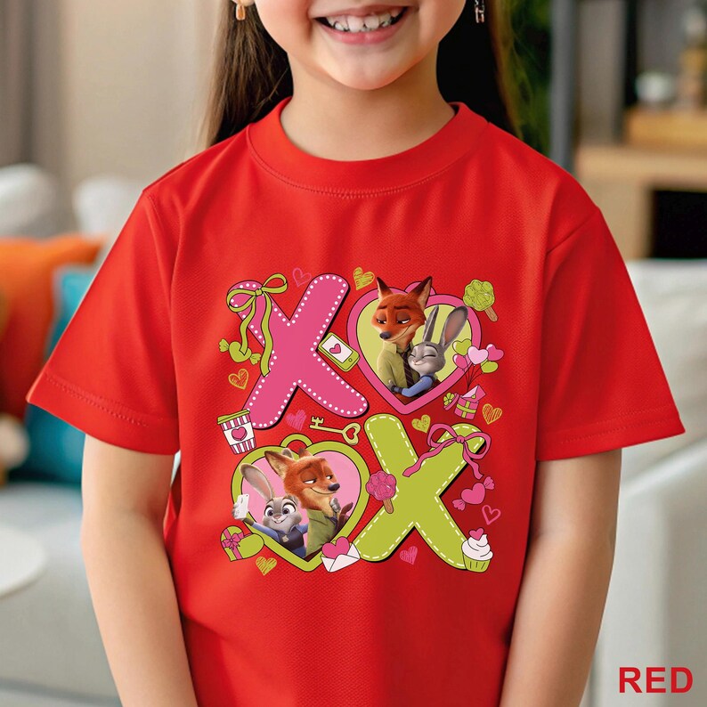 Peut inclure: Un t-shirt rouge &agrave; manches courtes avec une impression graphique des personnages Nick Wilde et Judy Hopps de Zootopie. Le motif comprend de grandes lettres X roses et vertes, des c&oelig;urs et de petites ic&ocirc;nes comme des cl&eacute;s et des cupcakes.