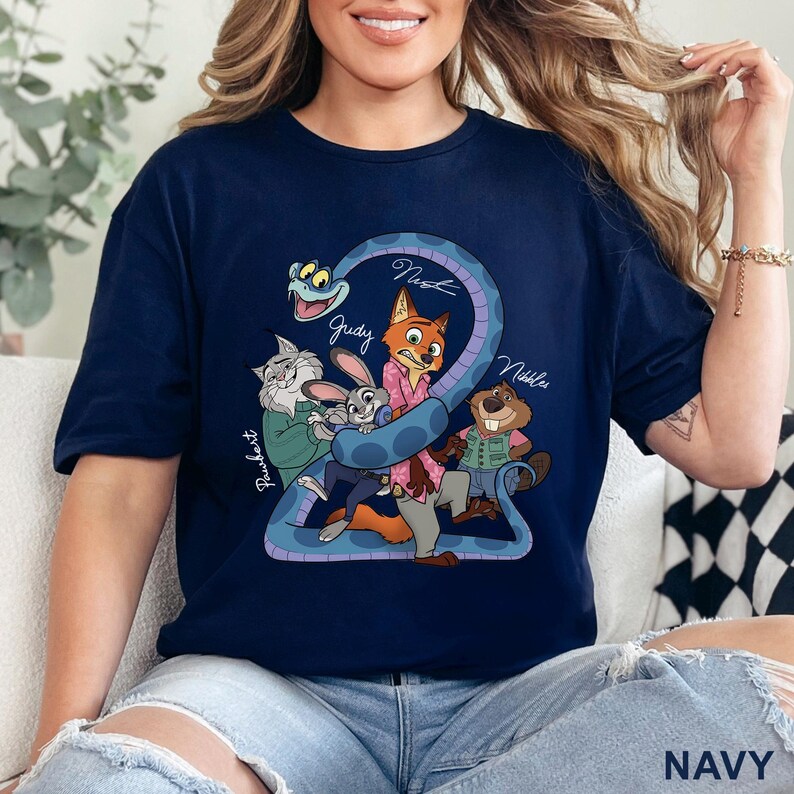 Puede incluir: Una camiseta azul marino de manga corta con un estampado gr&aacute;fico de personajes animados, incluyendo un zorro, un conejo, un gato, un castor y una serpiente. El texto "Judy", "Nick", "Pawbert" y "Nibbles" aparece junto a los personajes.
