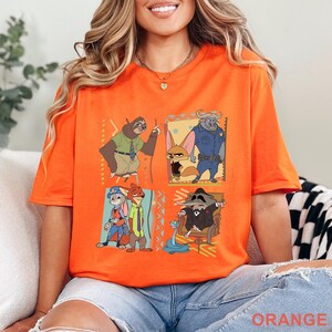 May include: Bright orange t-shirt with cartoon characters from Zootropolis. The design includes a sloth, fox, buffalo, rabbit, and a raccoon. The word "ORANGE" is printed at the bottom of the shirt.