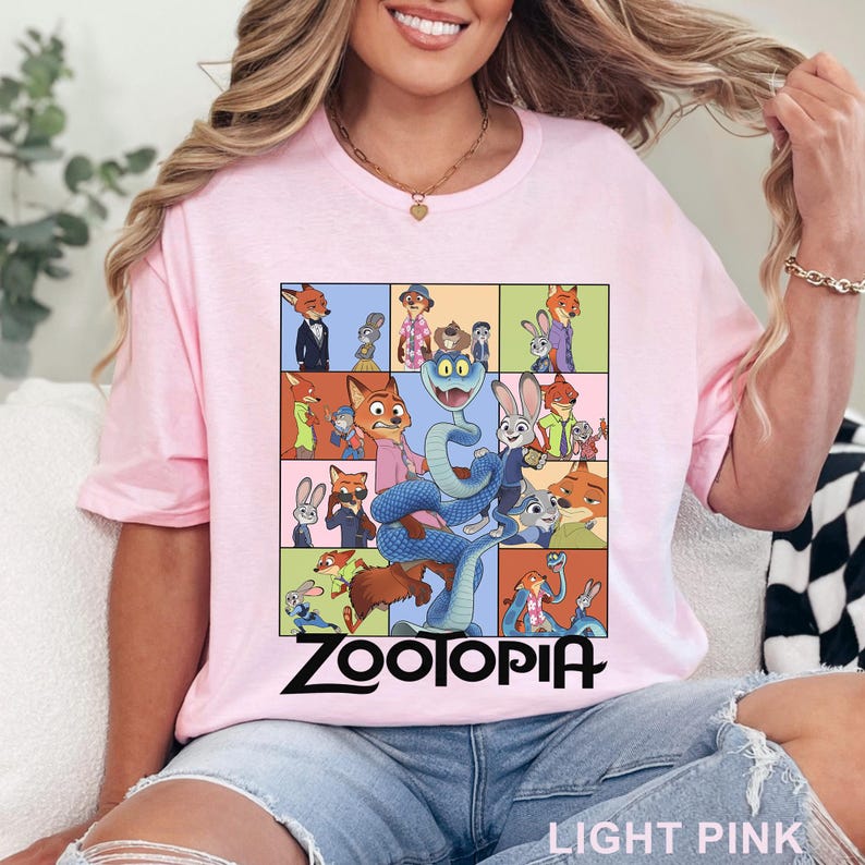 May include: A light pink t-shirt featuring a grid of various Zootopia character illustrations, including Nick Wilde and Judy Hopps, with a large blue snake in the centre. The word Zootopia is printed in bold black lettering below the graphic design.