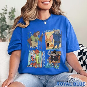 May include: Royal blue t-shirt with a cartoon graphic of animal characters from a popular animated film. The design features a sloth, fox, rabbit, and other characters in a square arrangement. The shirt is a relaxed, casual style.