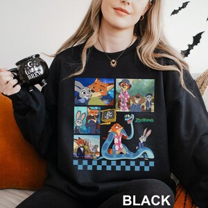 May include: Black sweatshirt featuring a colorful collage of characters from the animated movie "Zootopia." The design includes images of Judy Hopps, Nick Wilde, and other characters. The word "Zootopia" is printed in green, and the word "BLACK" is printed at the bottom.