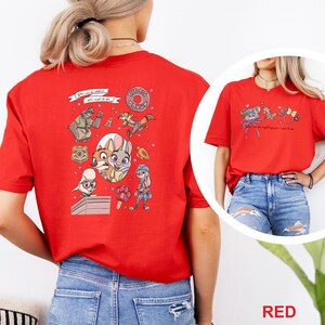 May include: A red t-shirt featuring a large graphic on the back with various cartoon characters, a donut, a badge, and a carrot. The front of the shirt displays a smaller graphic with mouse ears and text. The shirt is shown from the back and front.