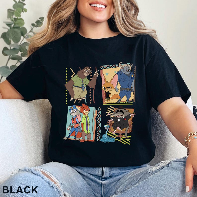 May include: Black t-shirt with a cartoon graphic of Zootopia characters in four panels with decorative borders. The word "BLACK" is printed at the bottom. The design features various characters from the animated film.