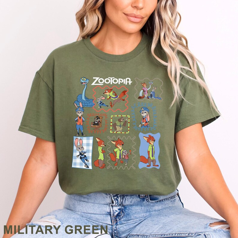 K&ouml;nnte beinhalten: Ein olivgr&uuml;nes Kurzarm-T-Shirt mit einem Grafikdruck des Zootopia-Logos und verschiedenen Charakteren aus dem Film, darunter Judy Hopps und Nick Wilde, angeordnet in einer Collage aus bunten, gemusterten rechteckigen Rahmen.