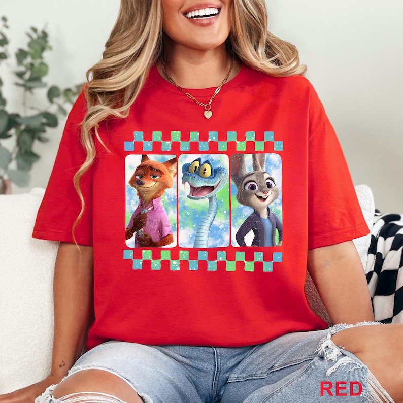 May include: Red t-shirt featuring a graphic of three animated characters in a film strip design. The characters include a fox, a snake, and a rabbit. The shirt is a solid red color.