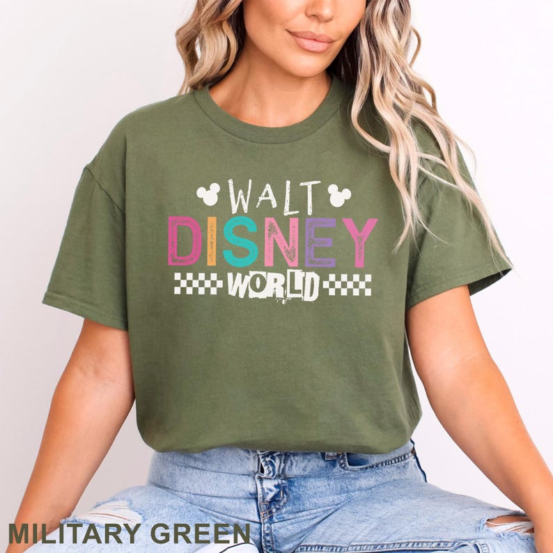 Pu&ograve; includere: Una t-shirt a maniche corte color verde oliva con la scritta WALT DISNEY WORLD in un carattere multicolore dall'aspetto vissuto. Il design include due piccole sagome bianche della testa di Topolino e un motivo a scacchi bianco sotto la parola WORLD.