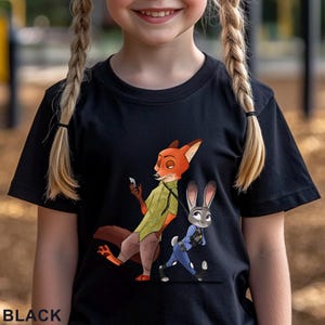 May include: Black t-shirt featuring a cartoon illustration of a fox and a rabbit. The fox is wearing a green shirt and holding a phone, while the rabbit is in a blue uniform. The word "BLACK" is printed at the bottom.