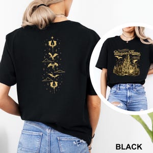 May include: Black t-shirt featuring a gold dragon design on the back and a gold castle graphic on the front. The front graphic includes the text "Riorrson House" and "Arctica". The shirt is made of a soft material.