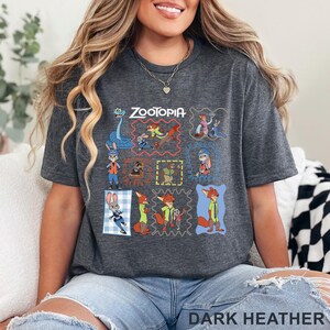 K&ouml;nnte beinhalten: Ein dunkelgrau meliertes Kurzarm-T-Shirt mit einem Grafikdruck verschiedener Zootopia-Figuren in bunten Rahmen. Das Design zeigt Judy Hopps und Nick Wilde in verschiedenen Posen, mit dem Zootopia-Logo in wei&szlig;em Druck am oberen Rand.
