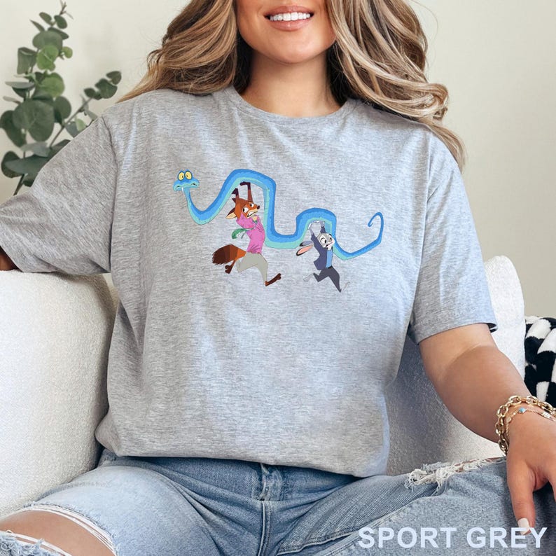 May include: A heather gray short-sleeve t-shirt featuring a graphic print of a long blue snake winding around a cartoon fox wearing a pink shirt and a cartoon rabbit wearing a blue blazer. The characters appear to be running in a state of alarm.