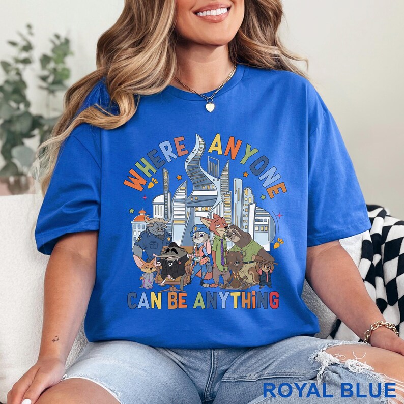 May include: Royal blue t-shirt featuring a colorful graphic of cartoon characters and a futuristic city. The text "WHERE ANYONE CAN BE ANYTHING" is displayed above the characters. The shirt is a comfortable, casual style.