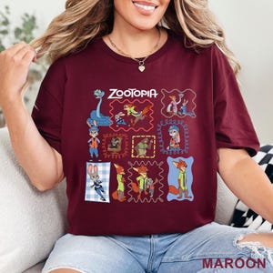 K&ouml;nnte beinhalten: Ein kastanienbraunes Kurzarm-T-Shirt mit einem Grafikdruck verschiedener Charaktere aus dem Film Zoomania. Das Design enth&auml;lt mehrere gerahmte Illustrationen von Judy Hopps, Nick Wilde und anderen Charakteren, mit dem Text Zootopia oben.