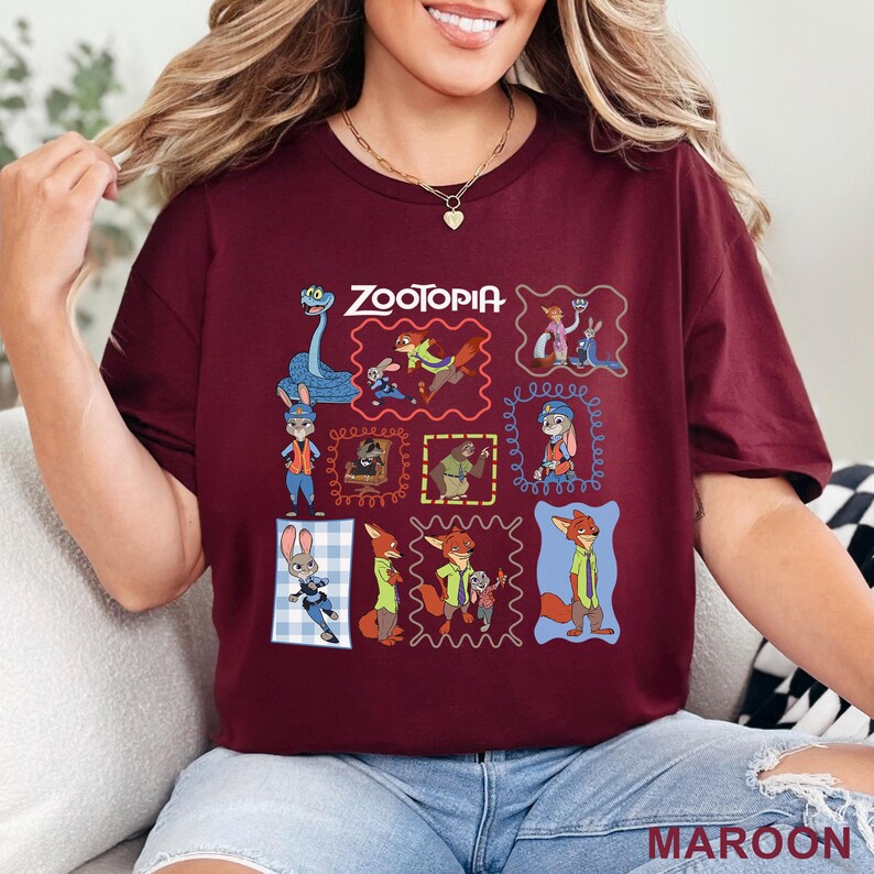 K&ouml;nnte beinhalten: Ein kastanienbraunes Kurzarm-T-Shirt mit einem Grafikdruck verschiedener Charaktere aus dem Film Zoomania. Das Design enth&auml;lt mehrere gerahmte Illustrationen von Judy Hopps, Nick Wilde und anderen Charakteren, mit dem Text Zootopia oben.