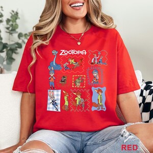 K&ouml;nnte beinhalten: Ein leuchtend rotes Kurzarm-T-Shirt mit dem Zootopia-Logo und einer Collage verschiedener Charakterillustrationen aus dem Film, darunter Judy Hopps und Nick Wilde, die in bunten rechteckigen Rahmen auf der Vorderseite angeordnet sind.
