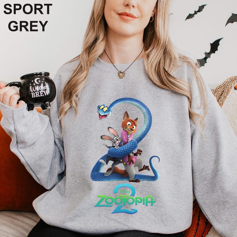 May include: Sport grey sweatshirt featuring a colorful graphic from the movie Zootopia 2. The design includes the characters Nick Wilde, Judy Hopps, and a blue snake. The word "Zootopia" is printed in green at the bottom.