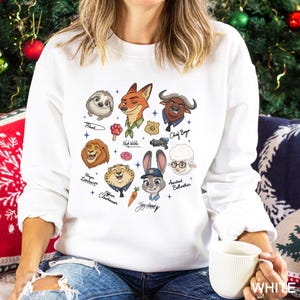 May include: White sweatshirt featuring cartoon illustrations of characters from Zootopia, including Flash, Nick Wilde, and Judy Hopps. The design includes character names and various related icons. The word "WHITE" is printed on the bottom right.